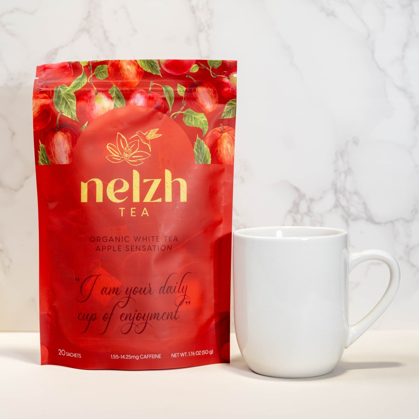 A bag of Nelzh Tea's Organic White Tea, Apple Sensation, standing next to a plain white mug. The tea bag is a vibrant red with an apple pattern and gold lettering.
